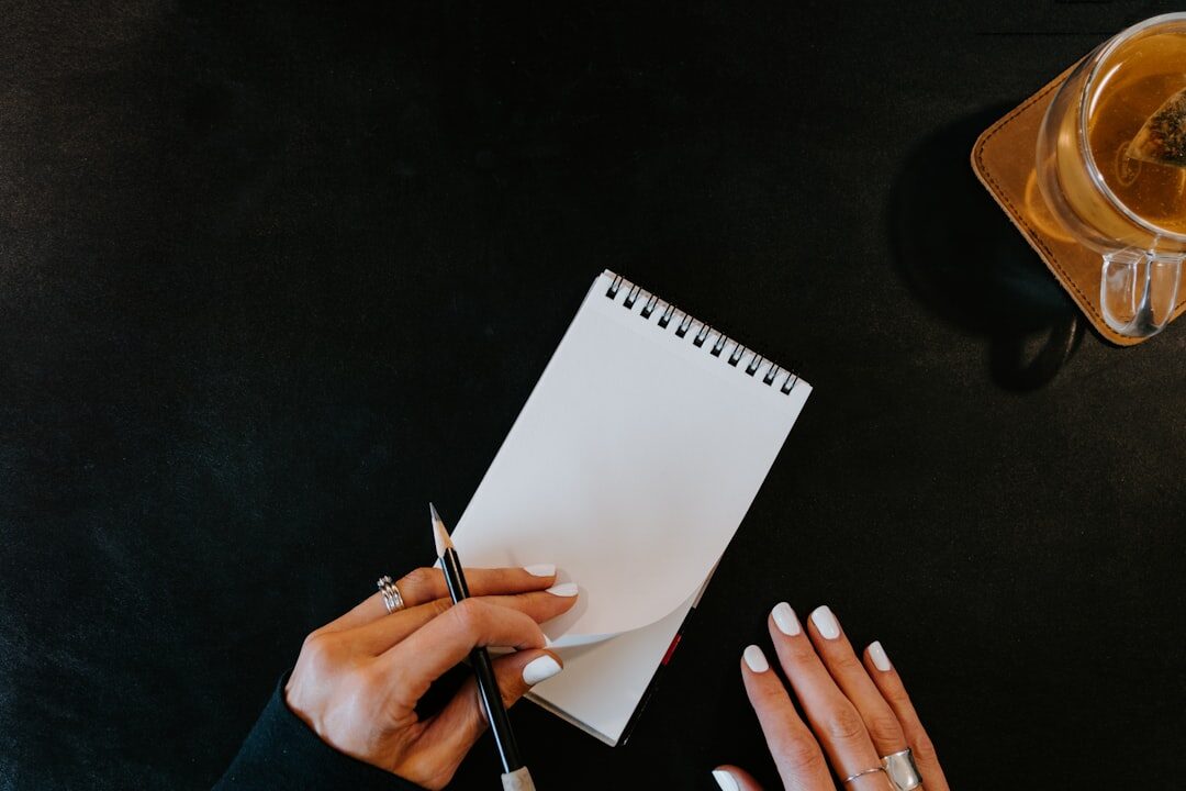 Hands writing in a notebook next to a laptop and coffee